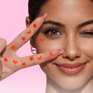 Woman making a peace sign with her fingers, surrounded by graphic eyeliner stamps on a pink background.