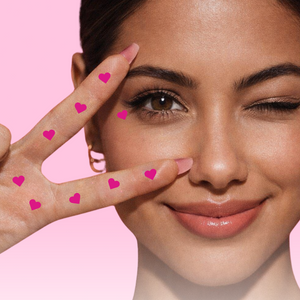 Woman making a peace sign with heart-shaped stickers on pink background, featuring 'Plot Twist' eyeliner product.
